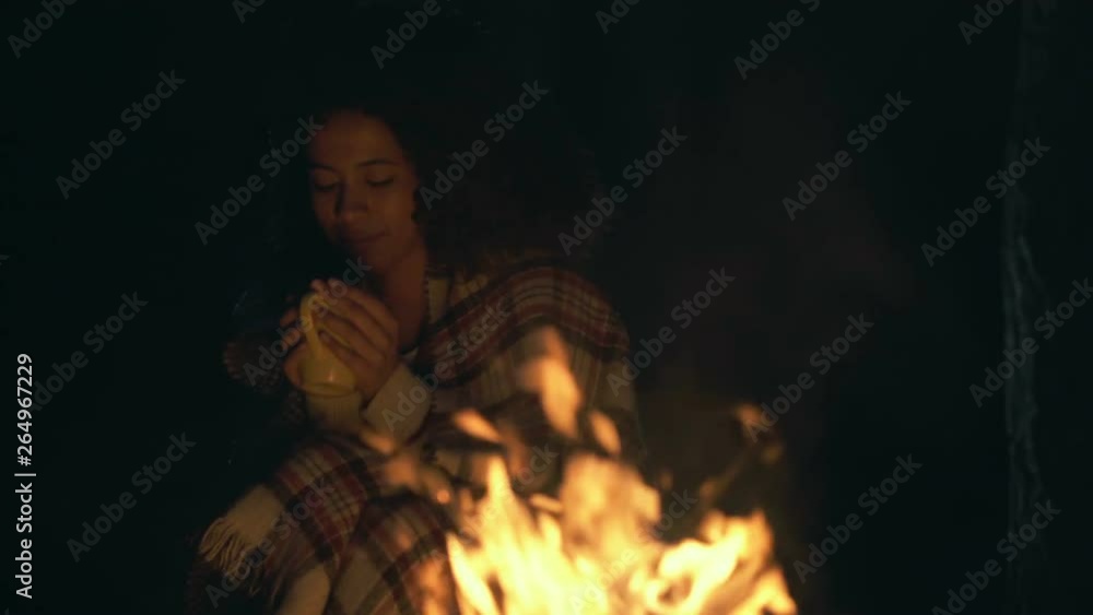 Young afro american woman sitting near the fireplace. Drinking tea (or coffee) and enjoying nice evening. Young afro american woman sitting near the fireplace. Drinking tea (or coffee) and enjoying nice evening.