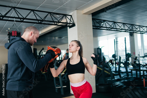 Young female boxing at gym with male instructor. Couple exercising punching
