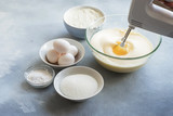 Mixer whipping eggs in a glass bowl and ingredients to create a cake 