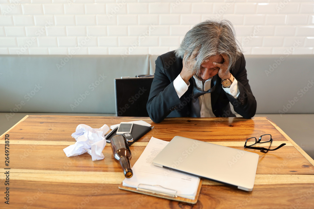 senior businessman got stress from failure in business with computer, cell phone, documents and alcohol bottle on wood table senior businessman got stress from failure in business with computer, cell phone, documents and alcohol bottle on wood table