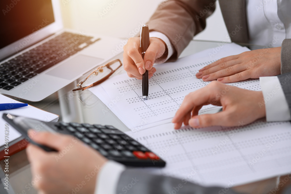 Two female accountants counting on calculator income for tax form completion hands close-up. Business and audit concept Two female accountants counting on calculator income for tax form completion hands close-up. Business and audit concept
