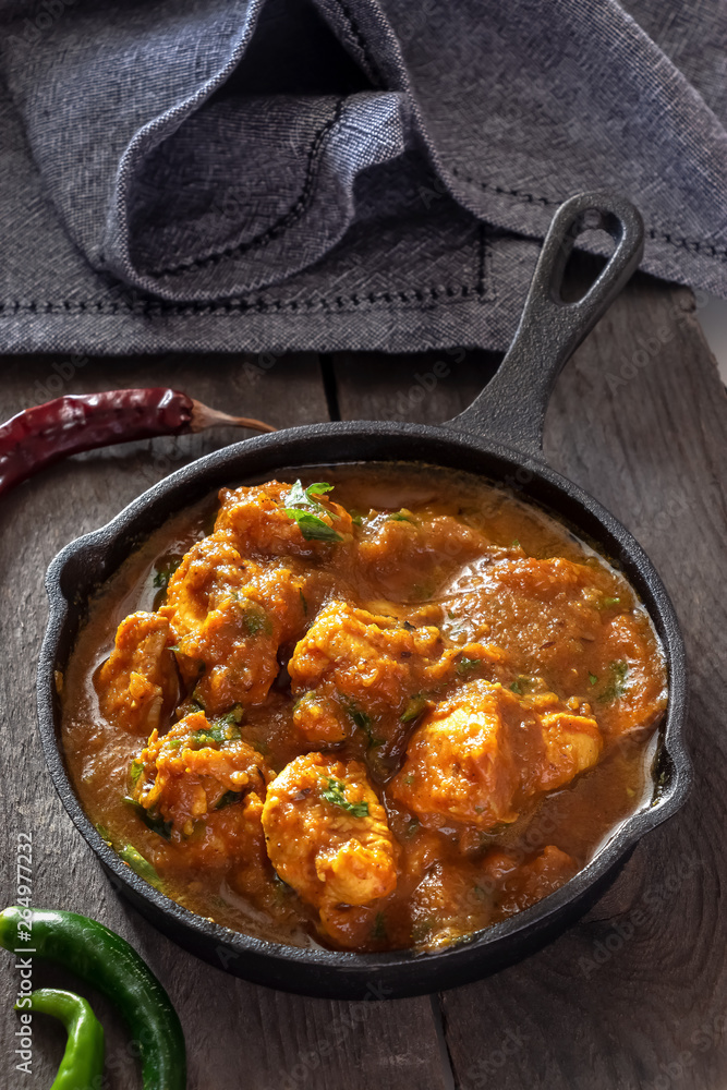 Close up traditional Indian butter chicken curry and lemon served with chapati bread in iron-cast. Wooden background.