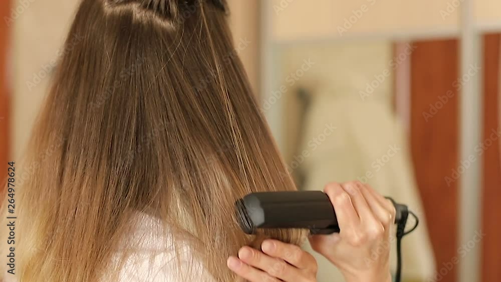 Hair care concept. Blonde woman straightening hair with hair straightener, rear view close-up slow motion Hair care concept. Blonde woman straightening hair with hair straightener, rear view close-up slow motion