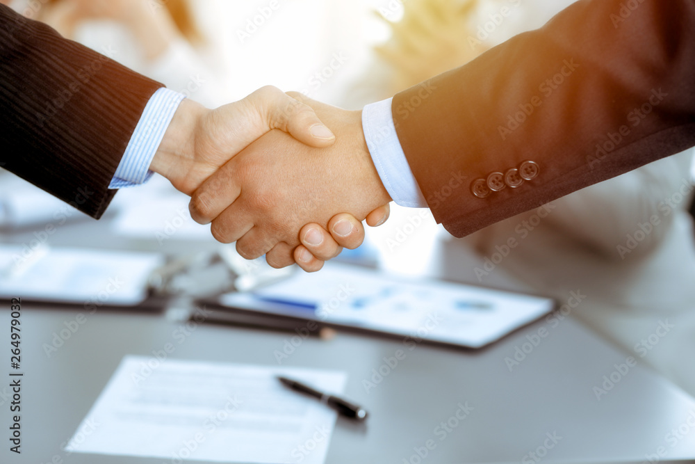Business people shaking hands at meeting while theirs colleagues clapping and applauding. Group of unknown businessmen and women in modern white office. Success teamwork, partnership and handshake Business people shaking hands at meeting while theirs colleagues clapping and applauding. Group of unknown businessmen and women in modern white office. Success teamwork, partnership and handshake