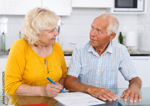 Smiling mature couple  in home interior filling up documents © JackF