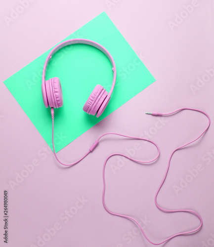 Pink headphones with cable on green-pink creative background. Minimalism. Top view