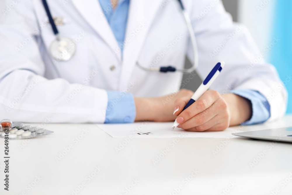 Female doctor filling up prescription form while sitting at the desk in hospital closeup. Healthcare, insurance and excellent service in medicine concept Female doctor filling up prescription form while sitting at the desk in hospital closeup. Healthcare, insurance and excellent service in medicine concept