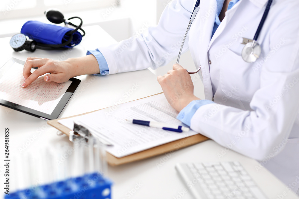 Doctor working table. Woman physician using tablet computer while sitting in hospital office close-up. Healthcare, insurance and medicine concept Doctor working table. Woman physician using tablet computer while sitting in hospital office close-up. Healthcare, insurance and medicine concept