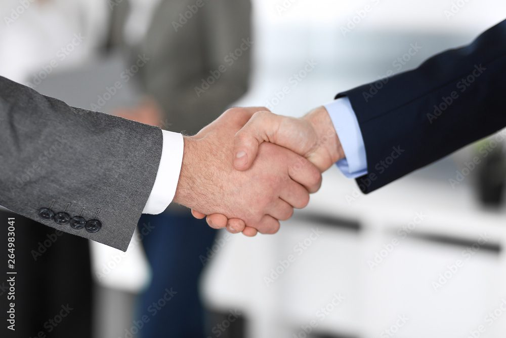 Business people shaking hands at meeting or negotiation, close-up. Group of unknown businessmen and women in modern office at background. Teamwork, partnership and handshake concept Business people shaking hands at meeting or negotiation, close-up. Group of unknown businessmen and women in modern office at background. Teamwork, partnership and handshake concept
