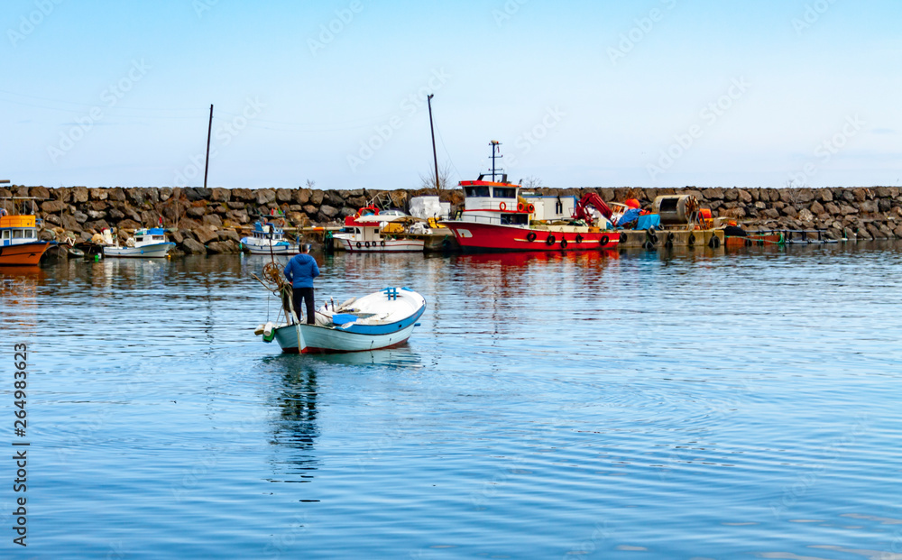 Colorful fishing boats in a harbour on a clear sunny day with blue skies reflected in the calm water.