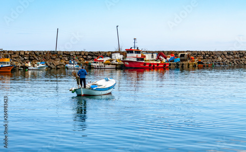 Colorful fishing boats in a harbour on a clear sunny day with blue skies reflected in the calm water.