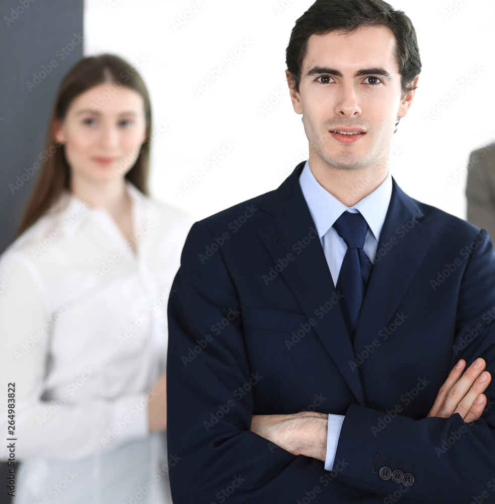 Headshot of businessman standing straight with colleagues at background in office. Group of business people discussing questions at conference or presentation. Success and business concept Headshot of businessman standing straight with colleagues at background in office. Group of business people discussing questions at conference or presentation. Success and business concept