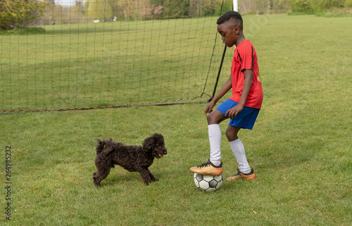 Hampshire, England, UK. April 2019. A young football player defending the goal during a traning session with his pet dog in a public park. photo