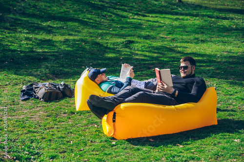 two men friends laying on yellow inflatable mattress reading books © phpetrunina14