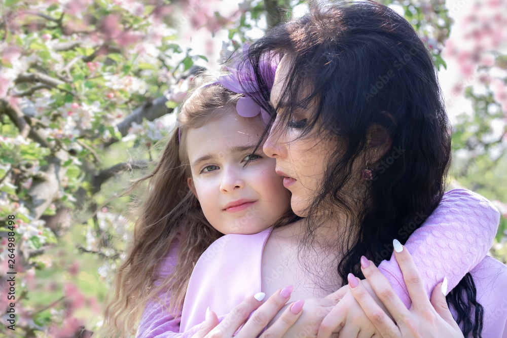 Fototapeta premium Mother and Daughter are walking in the blossoming apple orchard