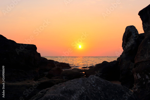 Pink sunset with bright yellow sun above the sea surface and rocks on coastline. Last colors the day on long beach Phu Quoc island, Vietnam. Summer vacation and travel is adventure concept background