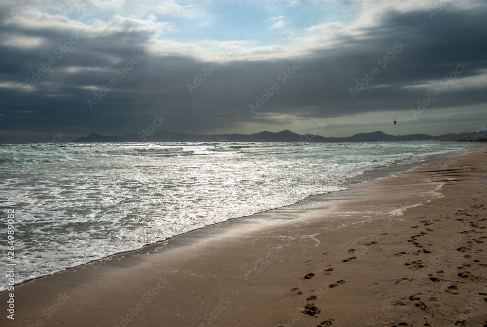 a kitesurfer surfs with a red kite on the beach of Mallorca a kitesurfer surfs with a red kite on the beach of Mallorca