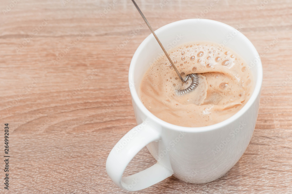 The recipe for delicious aromatic light coffee with milk and froth in a white cup on a wooden table in the kitchen for a good start to the day The recipe for delicious aromatic light coffee with milk and froth in a white cup on a wooden table in the kitchen for a good start to the day