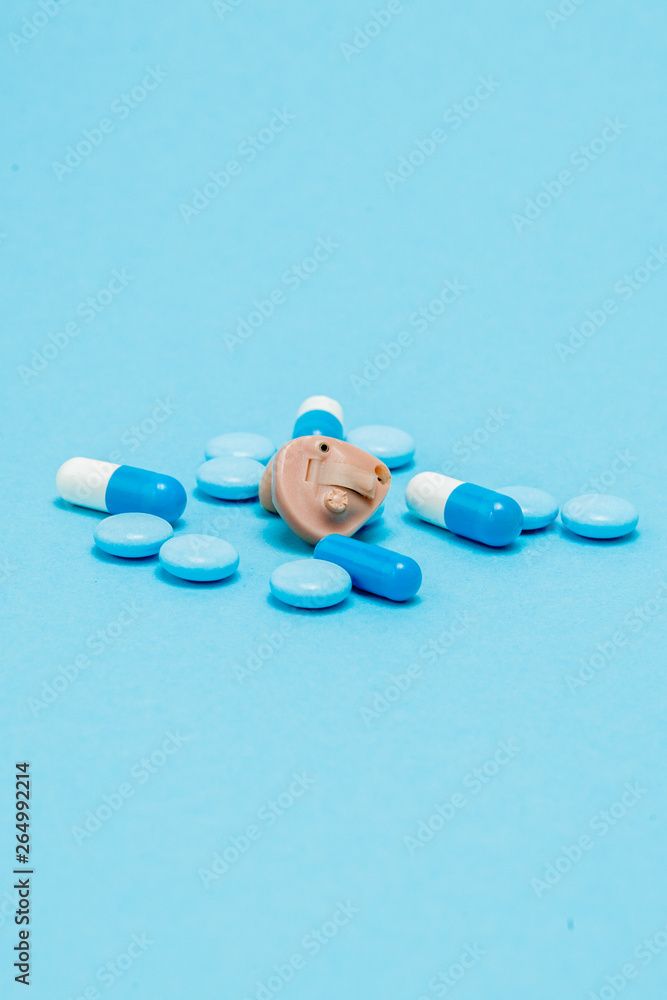 Hearing aid and blue pills on blue background. Medical, pharmacy and healthcare concept. Copy space. Empty place for text or logo Hearing aid and blue pills on blue background. Medical, pharmacy and healthcare concept. Copy space. Empty place for text or logo