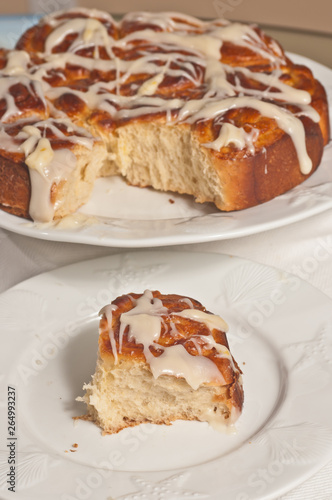 Top, front view, close distance of a freshly baked, homemade, slice of apricot, orange, sweet rolls, glazed with a vanilla frosting on a round, white plate  and rest in background