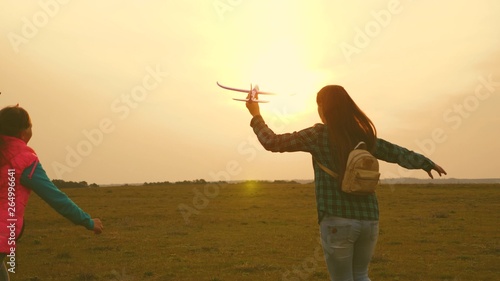 children play toy airplane. Happy girl sisters run with a toy plane at sunset on the field. The concept of a happy family. Girls dream of flying and becoming pilot. Slow motion