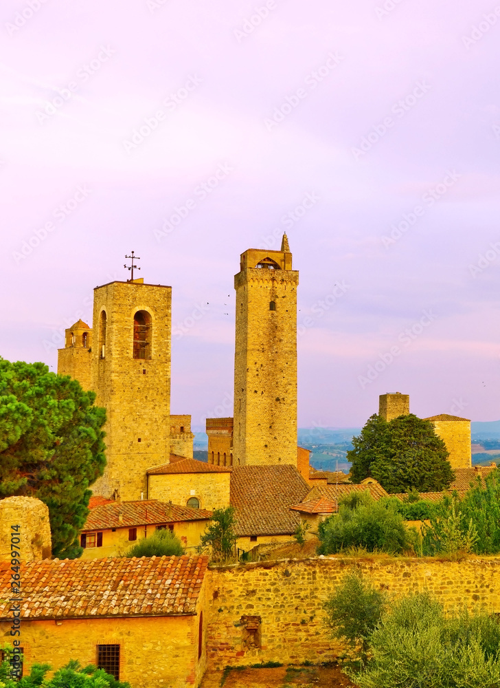View of the historic cityscape of San Gimignano facing the countryside in Tuscany, Italy at sunset.