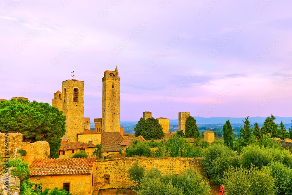 View of the historic cityscape of San Gimignano facing the countryside in Tuscany, Italy at sunset.
