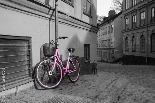 A picture of a lonely pink bike standing in the typical street in Stockholm. The bike looks to be modern in a retro style. The background is black and white. 