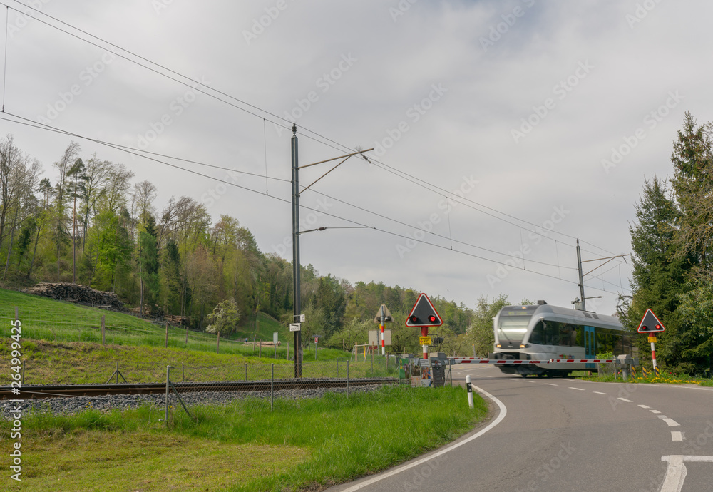 Steckborn, TG / Switzerland - 22 April 2019: railroad crossing in springtime countryside with a train speeding across a two lane road
