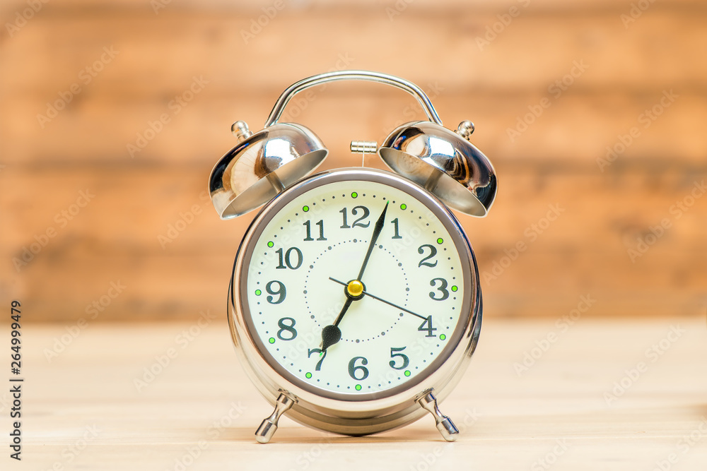 Silver alarm clock in retro style on a wooden background close-up shows 7 am Silver alarm clock in retro style on a wooden background close-up shows 7 am