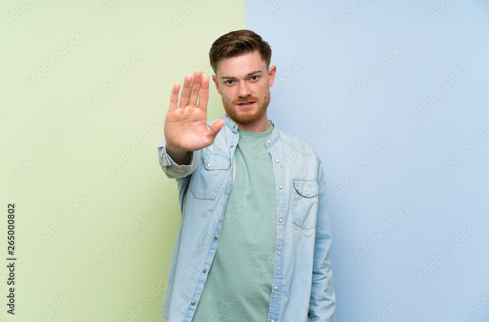 Redhead man over colorful background making stop gesture Redhead man over colorful background making stop gesture