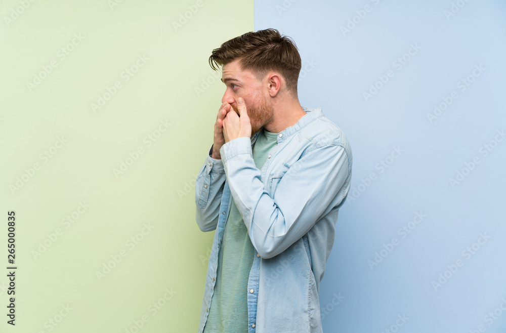 Redhead man over colorful background covering mouth and looking to the side Redhead man over colorful background covering mouth and looking to the side