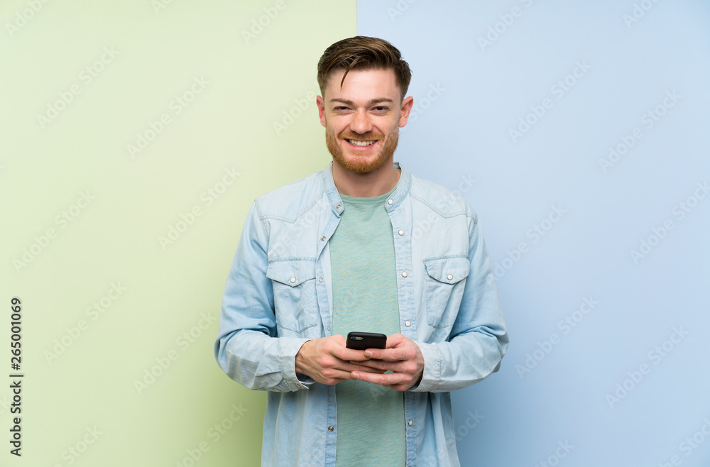 Redhead man over colorful background sending a message with the mobile Redhead man over colorful background sending a message with the mobile