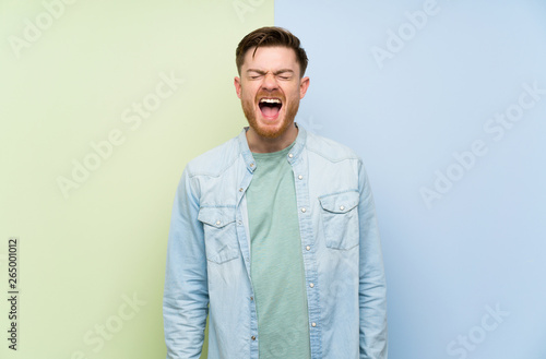 Redhead man over colorful background shouting to the front with mouth wide open
