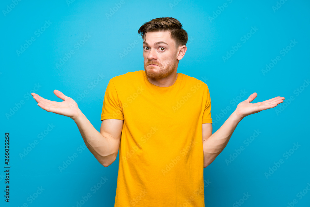 Redhead man over blue wall making doubts gesture Redhead man over blue wall making doubts gesture