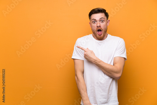 Redhead man over brown wall surprised and pointing side