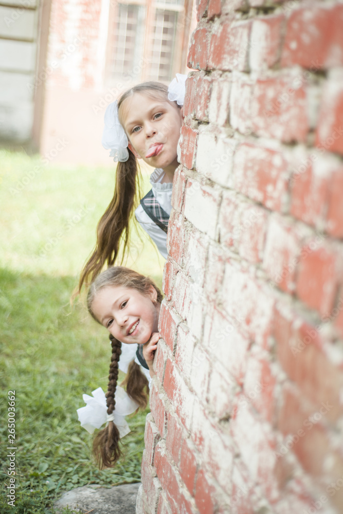 Two young schoolgirls, peeking out from behind a brick wall. Two young schoolgirls, peeking out from behind a brick wall.