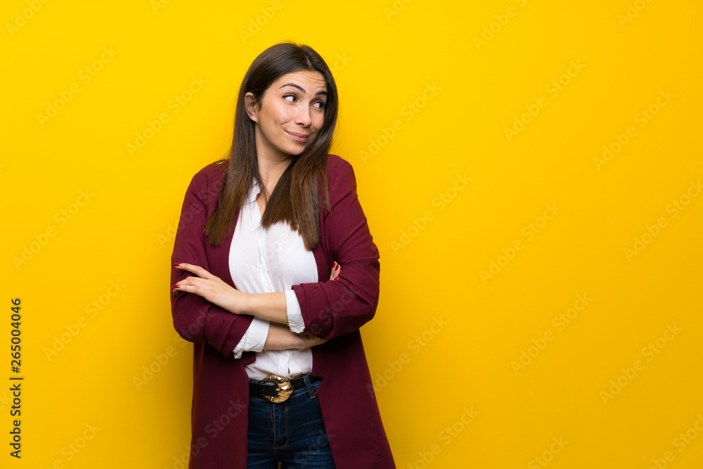 Young woman over yellow wall making doubts gesture while lifting the shoulders Young woman over yellow wall making doubts gesture while lifting the shoulders