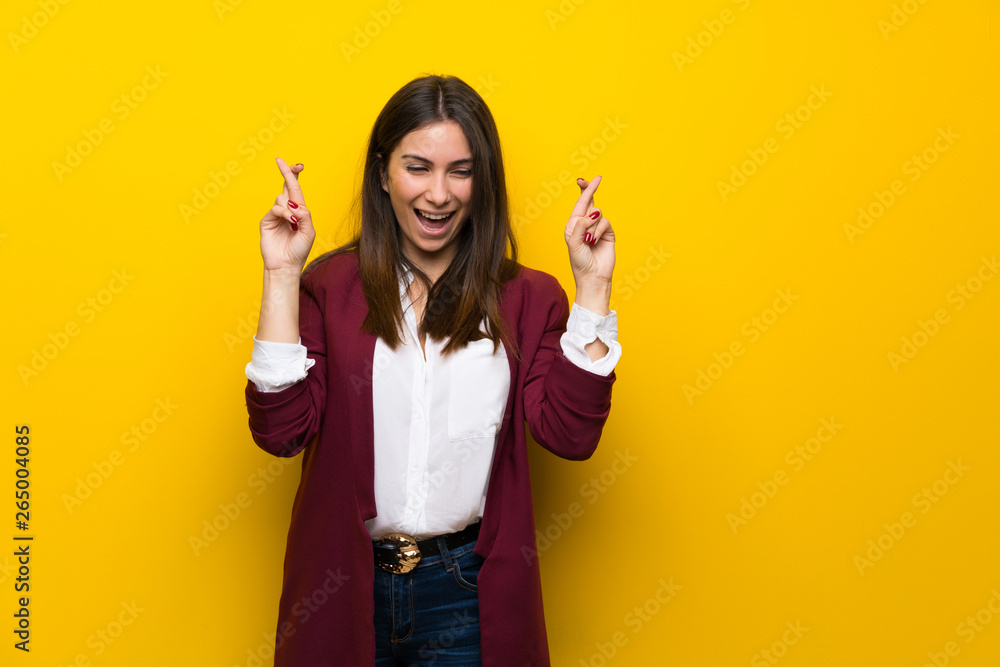 Young woman over yellow wall with fingers crossing Young woman over yellow wall with fingers crossing