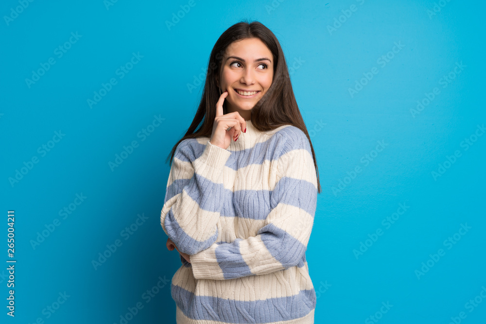Young woman over blue wall thinking an idea while looking up Young woman over blue wall thinking an idea while looking up