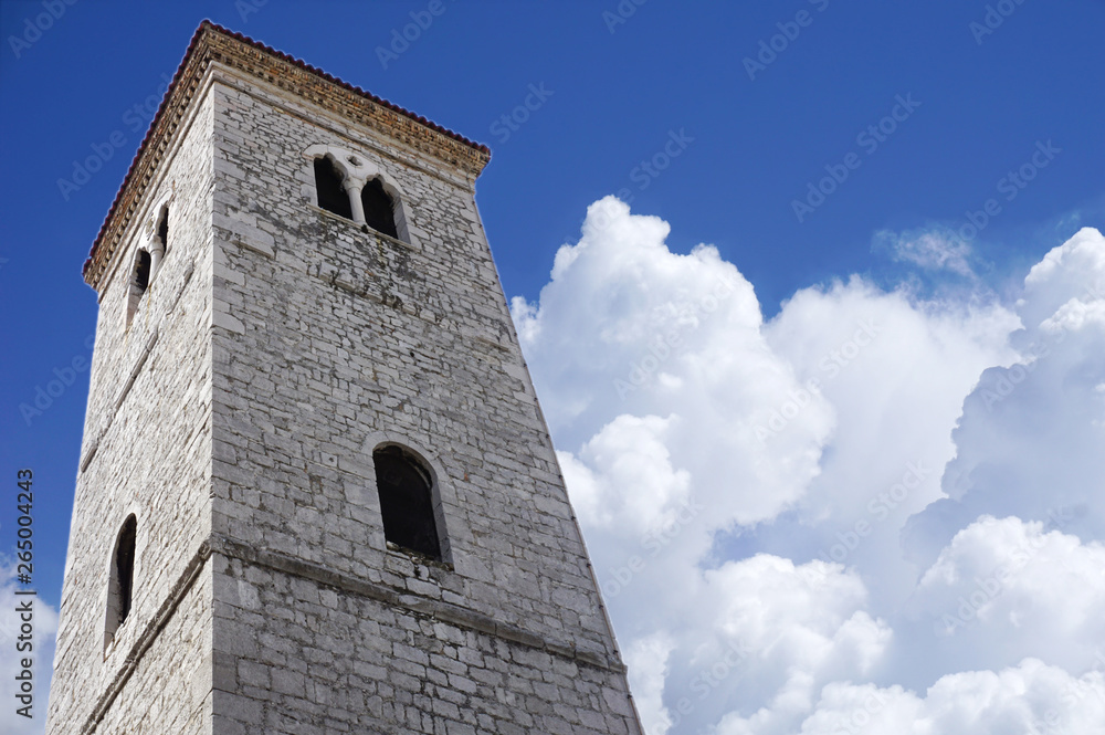 Old stone bell tower, a view from below, with a background of blue sky and snowy white clouds