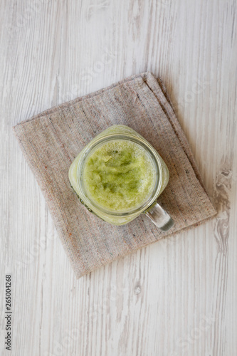 Green celery smoothie in a glass jar over white wooden background. Overhead, flat lay, from above.