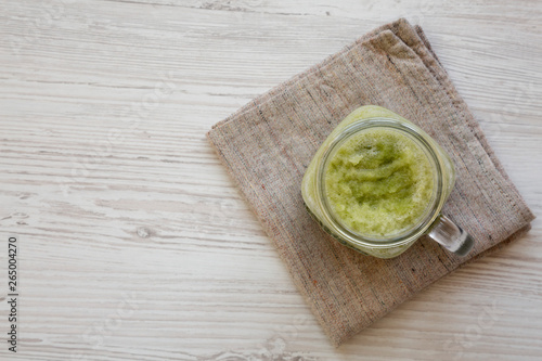 Green celery smoothie in a glass jar over white wooden surface. Overhead, flat lay, from above. Copy space.