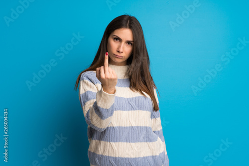 Young woman over blue wall making horn gesture