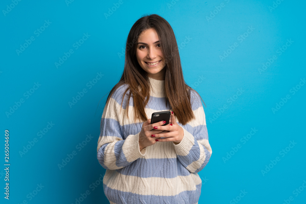 Young woman over blue wall sending a message with the mobile Young woman over blue wall sending a message with the mobile
