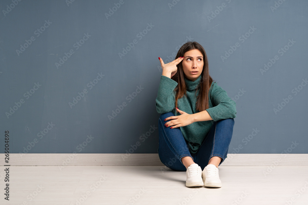 Young woman sitting on the floor with problems making suicide gesture