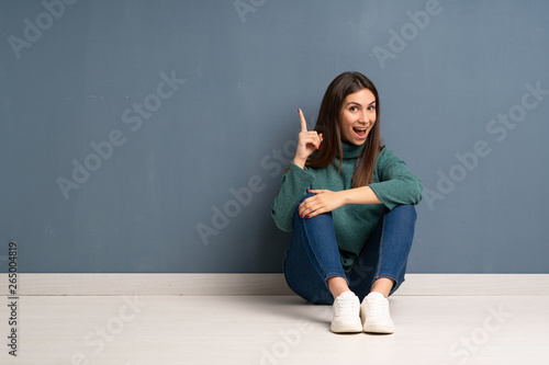 Young woman sitting on the floor intending to realizes the solution while lifting a finger up