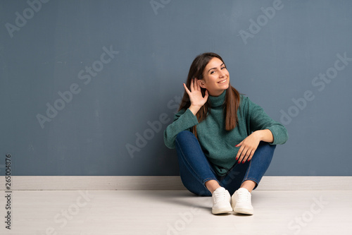 Young woman sitting on the floor listening to something by putting hand on the ear