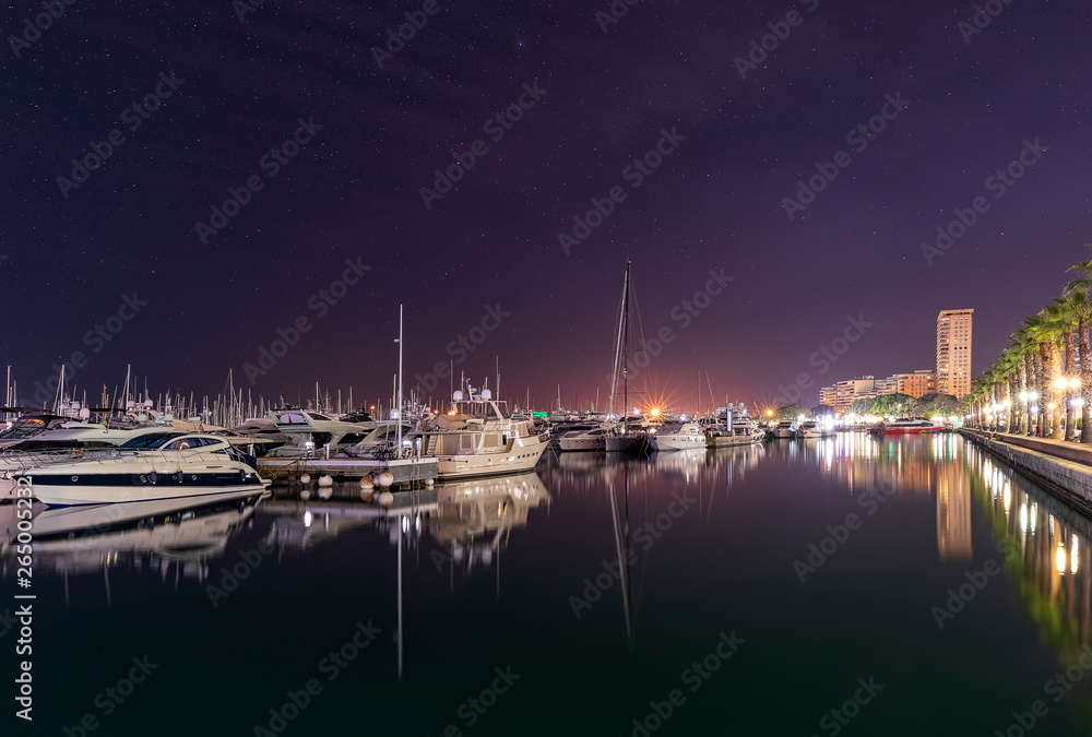 Marine port in Alicante at night. Luxury yachts, ships and fishing boats are standing in rows in harbor. Costa Blanca, Spain, Mediterranean sea. Main focus on boats. Long exposure photo. Soft light