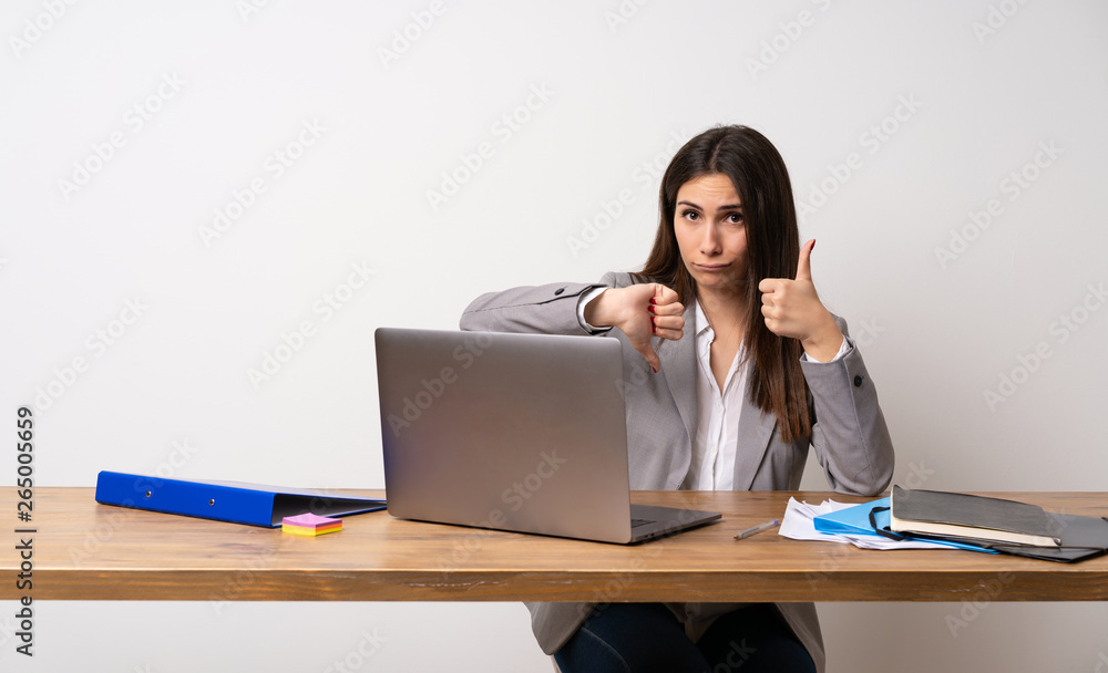 Business woman in a office making good-bad sign. Undecided between yes or not Business woman in a office making good-bad sign. Undecided between yes or not